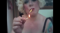 Una bionda amante retrò che fuma una sigaretta gialla Sobranie con un fiammifero acceso