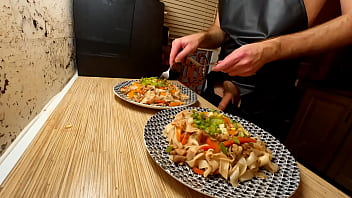 Cucina sexy. Lo chef gay nudo sta cucinando spaghetti di riso con pollo e verdure